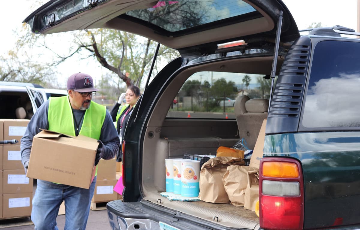Volunteers help direct traffic and load groceries into cars at the Community Food Bank’s new drive-through food distribution in Tucson