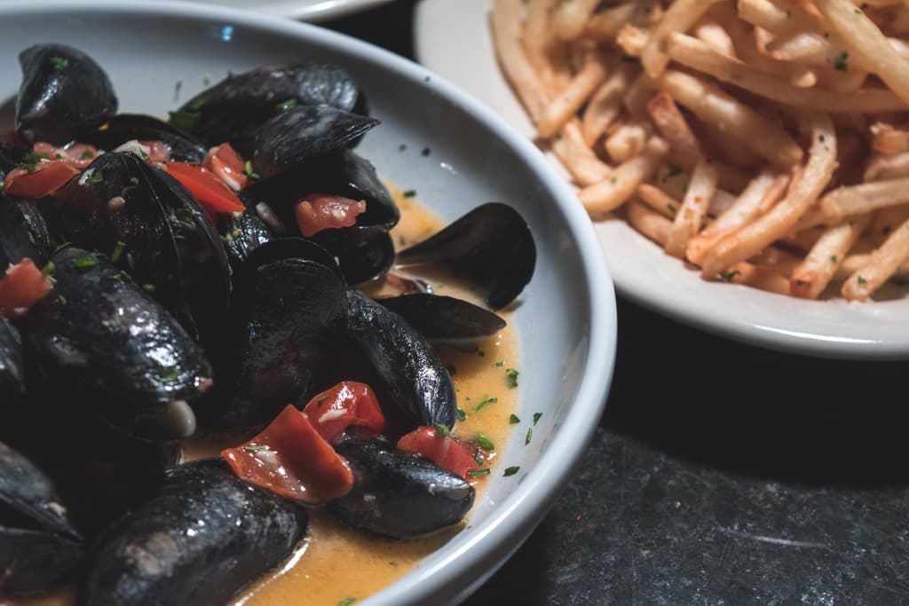 Steamed Prince Edward Island Mussels in a white wine garlic tomato beurre blanc and Roasted Garlic Fries at Wild Garlic Grill (Credit: Adam Lehrman)