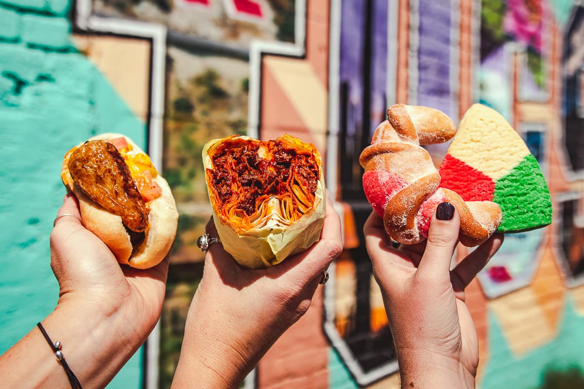 Sonoran hot dog, red chile burro, and pan dulce from Anita Street Market in front of the Greetings from Tucson Mural (Credit: Jackie Tran)