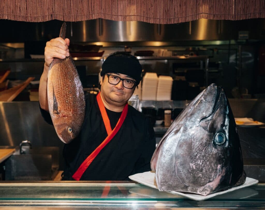 Sushi chef Jun Arai holding up a fish at the sushi bar