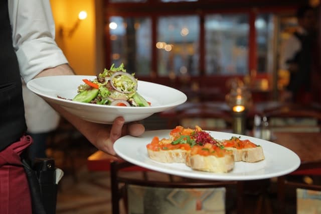 (pexels/<a href="https://www.pexels.com/photo/black-and-white-alcohol-bar-barkeeper-5373/" target="_blank">PIXABAY</a>) Food on two plates in a chef's hand