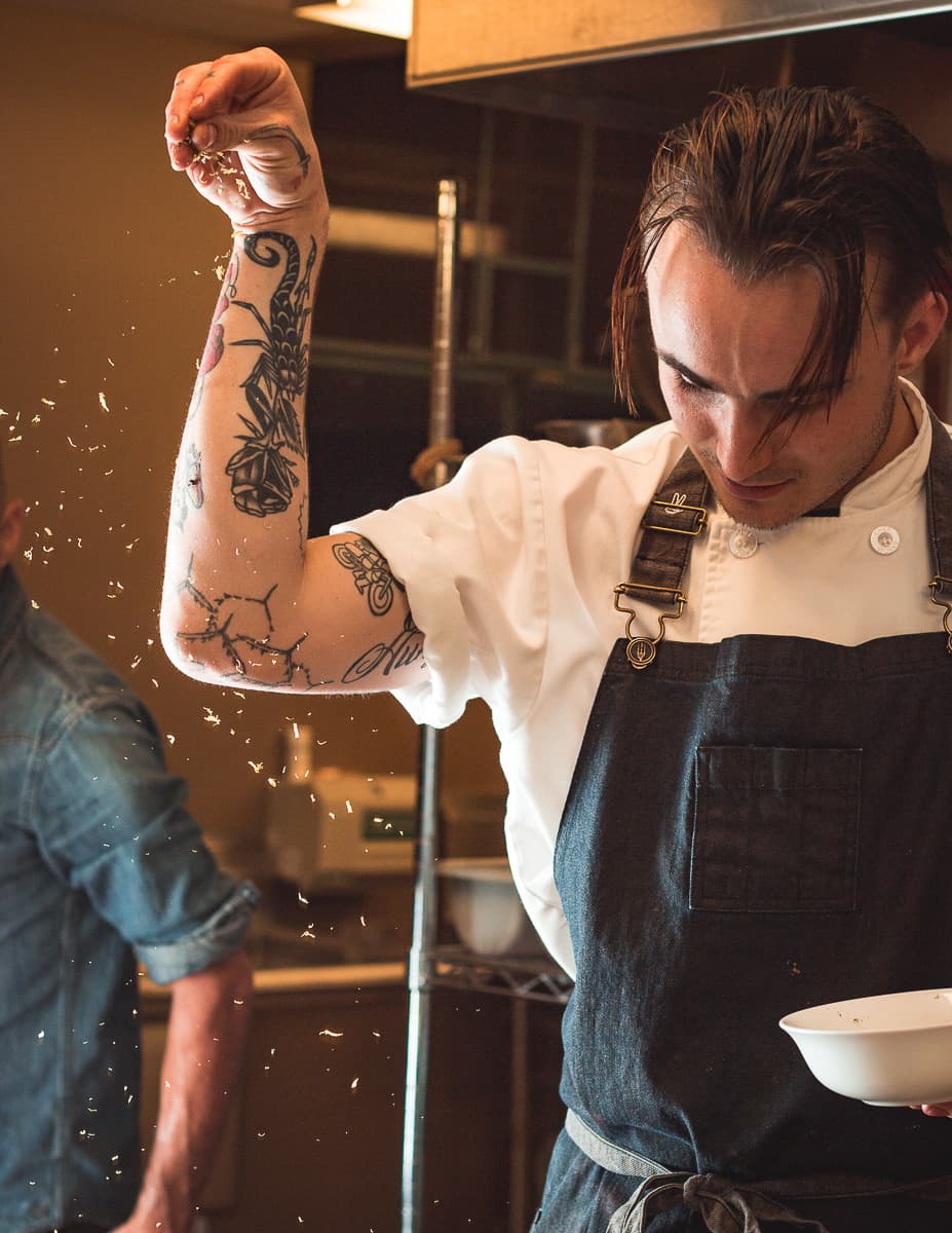 Chef Aidan Gould sprinkling candied lime zest a la Salt Bae onto his deconstructed tarta de merengue with grapefruit lavender custard, lime merengue, candied lime zest, and edible flowers at Blue Sky Cafe at Sky Islands Public High School (Credit: Jackie Tran)