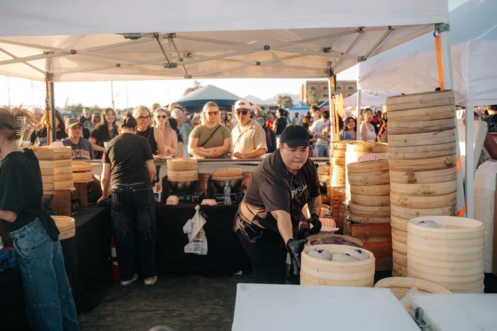 Staff serve a line of customers from a stall stacked with bamboo steamers.