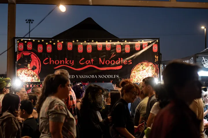 A crowd lines up at dusk at Chonky Cat Noodles, a stall strung with red paper lanterns.