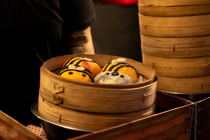 Bee-shaped steamed buns in a bamboo steamer basket at a stall.