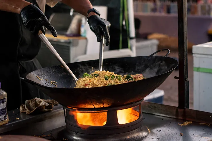 Noodles tossed in a wok over open flames at a food stall.
