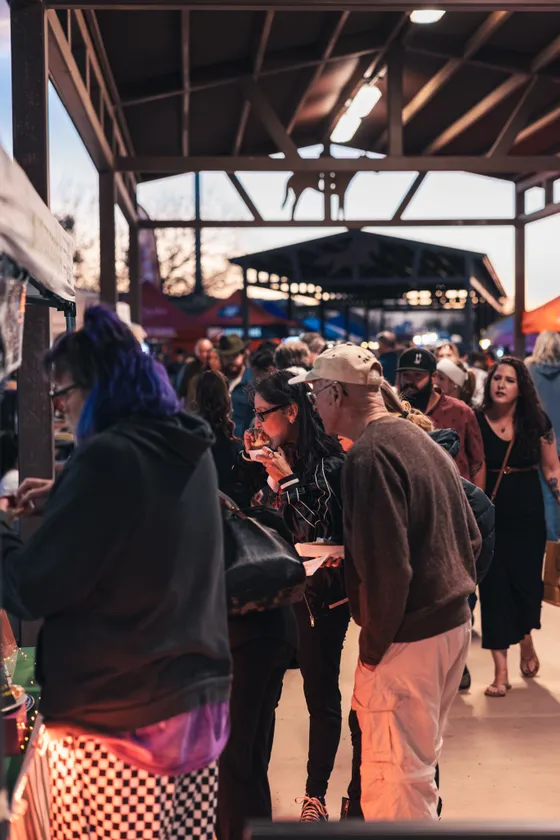 Attendees eating under the pavilion at dusk, string lights overhead.