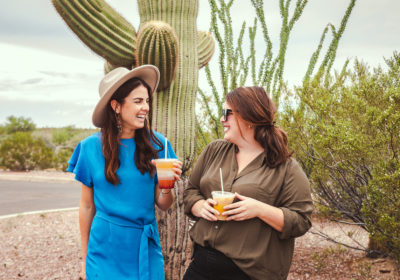 Tucson women laughing with their Presta Coffee beverages in front of a saguaro at Pima Community College West Campus in Tucson, Ariz.