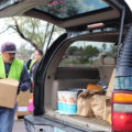 Volunteers help direct traffic and load groceries into cars at the Community Food Bank’s new drive-through food distribution in Tucson