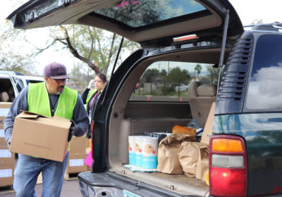 Volunteers help direct traffic and load groceries into cars at the Community Food Bank’s new drive-through food distribution in Tucson