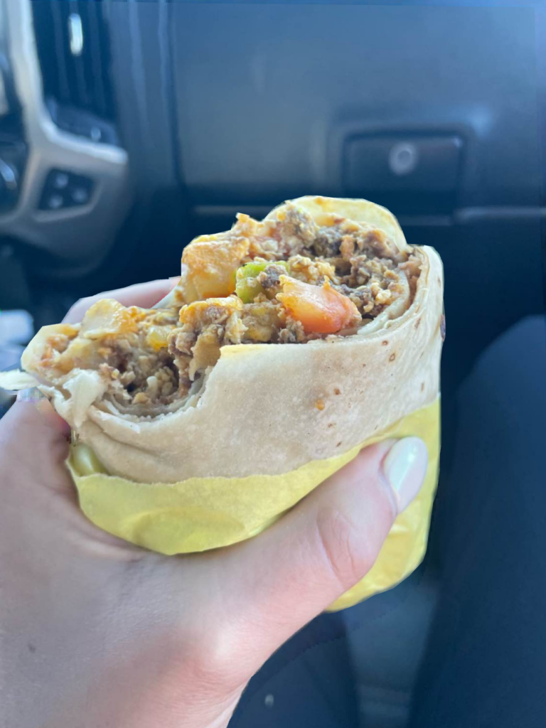 a hand holding a burrito in a car